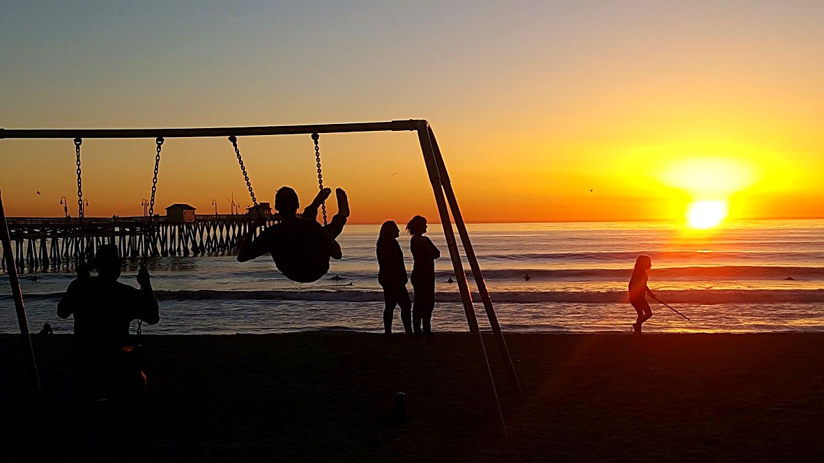 Kids on the beach swings at sunset with San Clemente Pier behind